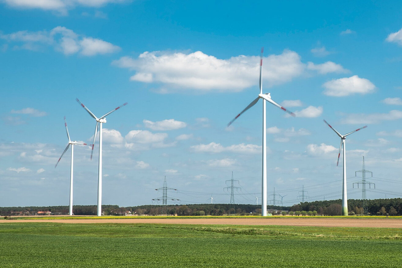 Ökostrom für ökologischen Betrieb Windkrafträder auf einer grünen Wiese. Im Hintergrund eine Stromtrasse und Berge